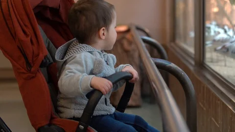A small child/boy sits in a dark red stroller.  Stock Footage 107000057