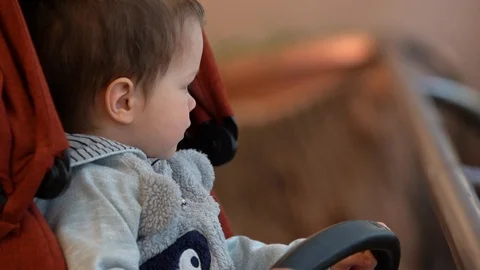 A small child/boy sits in a dark red stroller.  Stock Footage 107000124