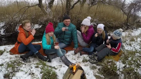Small children sit by the fire and drink tea in the winter forest. Video stock 61404141