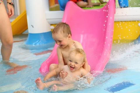 Small children sliding down the slide in the pool of water park Stock Photos