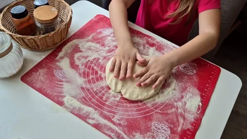 Small children's hands pouring flour and kneading dough on a red silicone mat Stock Footage 302253774