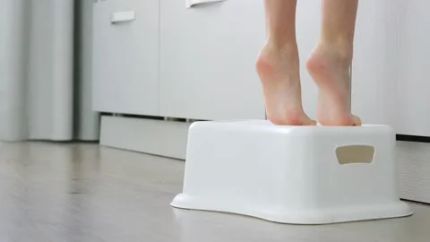 Small children's legs stand on a special children's stand on kitchen Stock Footage 231294148