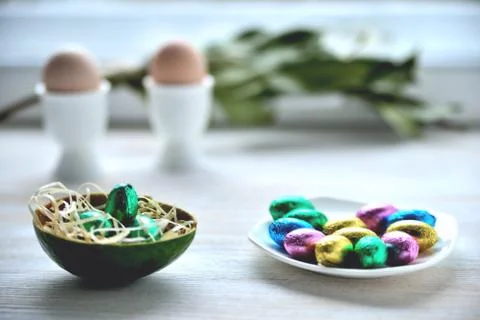 Small chocolate eggs in colored wrapper on saucer, two eggs in stands in the  Stock Photos