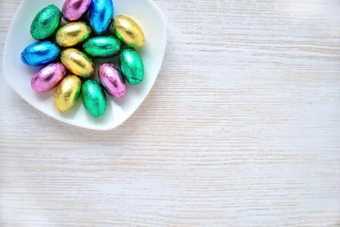 Small chocolate eggs in colored wrappers on saucer, place for inscription Stock Photos