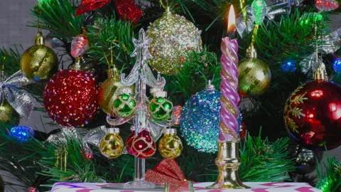 Small christmas tree and burning candle near green christmas tree with big balls Stock Footage 145074964