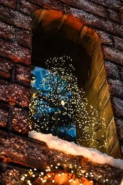 A small Christmas tree stands on the window of a brick building. New Year Stock Photos