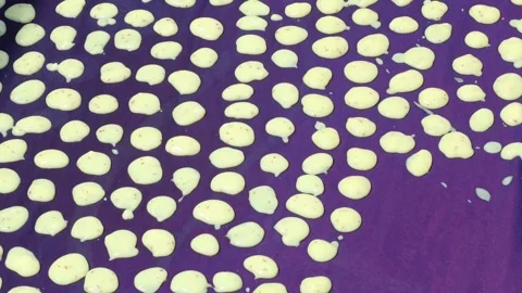 Small circles of liquid rice batter being carefully placed on a purple fabric Stock Footage 332408902