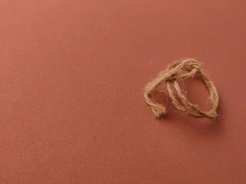 A small, circular loop of natural twine is tied into a simple knot on a red.. 写真素材