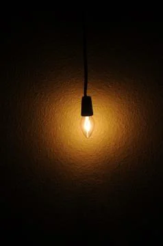 A small clear light bulb hanging next to a wall Stock Photos