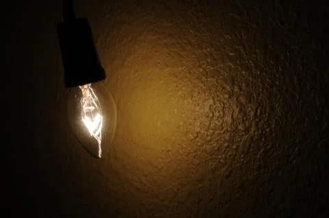A small clear light bulb hanging next to a wall Stock Photos