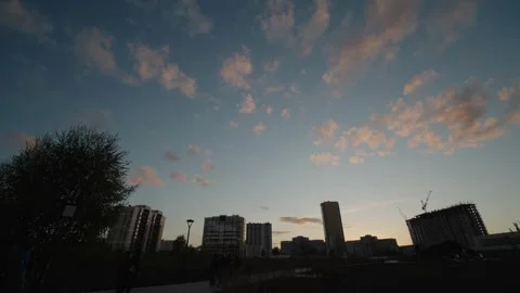 Small clouds glowing pink drifting over city buildings at sunset Stock Footage 334627654