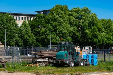 Small construction traktor and building materials stacked near a metal fence Stock Photos