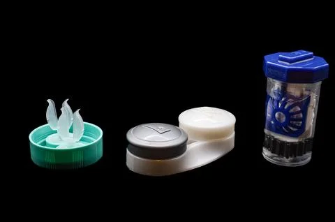 A small container of contact lens solution sits on a table next to a contact len Stock Photos