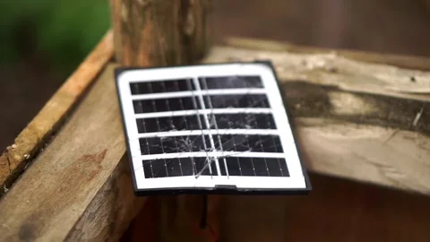 A small, cracked portable solar panel is placed on top of an outdoor wooden Stock-Footage 344329173