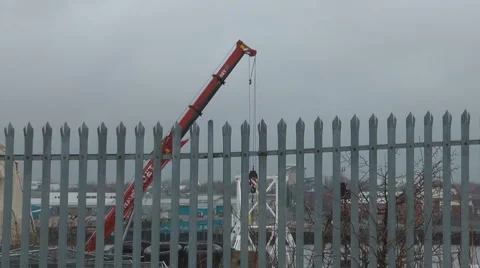 Small crane lifting metal in ship yard, seen through metal fence. Stock Footage 1090661