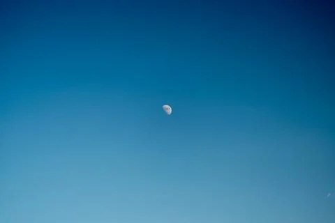 Small crescent moon high in clear blue sky with subtle color gradient Stock Photos