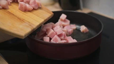 Small cubes of meat are placed into a frying pan as a person stirs and cooks. 库存影片 338298372