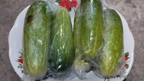 Small cucumber in plastic wrap on a white plate Stock Footage 219200139