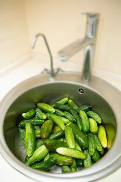 Small cucumbers are washed in the kitchen sink Foto stock