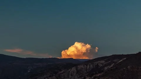 Small cumulus cloud erupting behind a mountain with sunset colors HD H264 Stock Footage 310452098