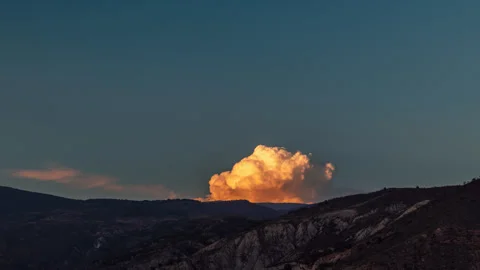 Small cumulus cloud erupting behind a mountain with sunset colors 4K ProRes 4444 Stock Footage 310452800