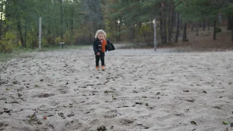 A small, curly-haired boy runs across the sand to the toy Stock Footage 100316379