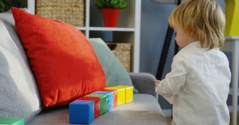 Small cute blonde boy playing with colourful cubes on the grey sofa and puttung Stock Footage 82917055