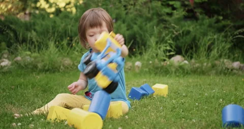 Small cute child is playing with toy car and cubes sitting on green grass Stock Footage 159970314