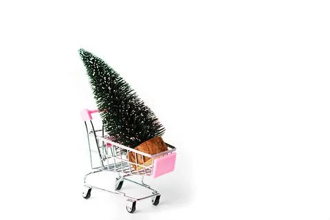 A small decorative Christmas tree lies in a shopping cart on a white backgrou Foto stock