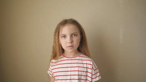 Small despairing kid looking into camera against the background of wall Видео 334926143