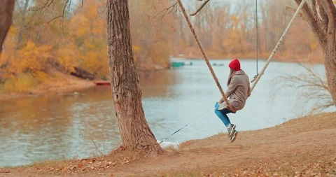 Small dog is standing by the river, and the mistress is swinging on a swing 스톡 동영상 118167845
