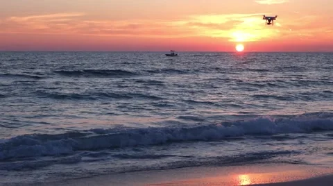 Small drone passes boat flying at sunset on the beach Video stock 56947567
