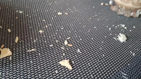 Small dry bread crumbs scattered across a dark textured placemat surface Stock Photos