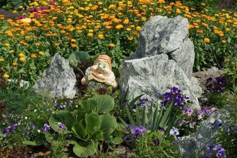 A small dwarf peeks out from behind the grass between the stones around the f 스톡 사진