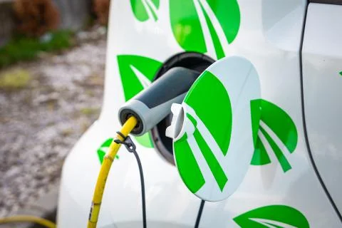 Small electric car with leafs on the side being charged up on a street. Stock Photos