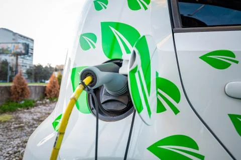 Small electric car with leafs on the side being charged up on a street. Stock Photos