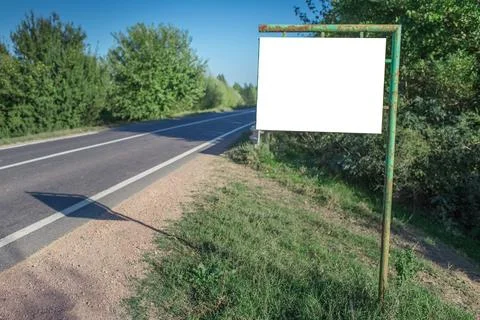 Small empty blank billboard mockup, near asphalting road in the woods. Stock Photos