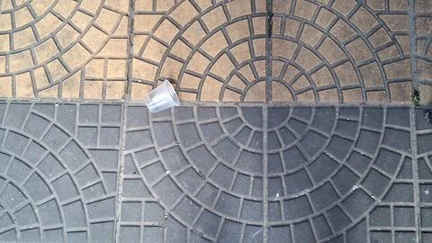 Small empty clear plastic cup discarded on textured stone pavement Stock Photos