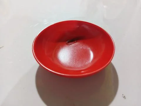Small empty red plastic sauce bowl on a white table surface. Stock Photos