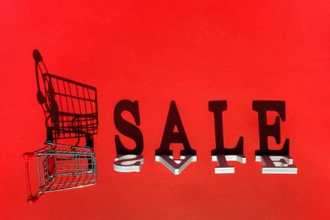 Small empty shopping trolley cart and word SALE of white letters casts a larg Stock Photos