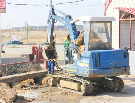 A small excavator digs a pit to replace the pipes. Stock Photos