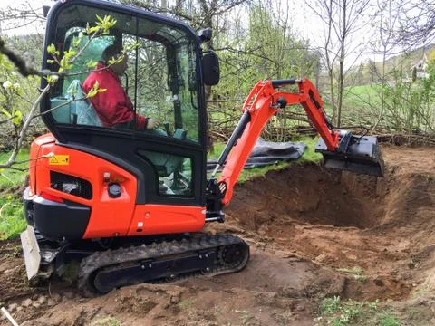 Small excavator with man inside, at work making garden pond Stock Photos