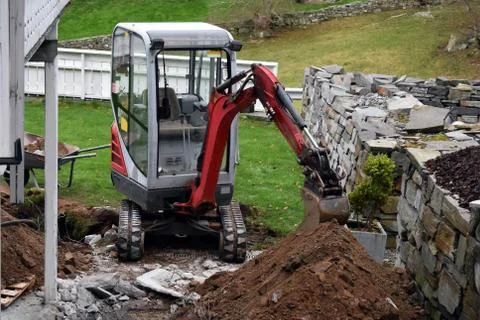 Small excavator without a driver in the cabin. Next is a broken road tile. Stock Photos
