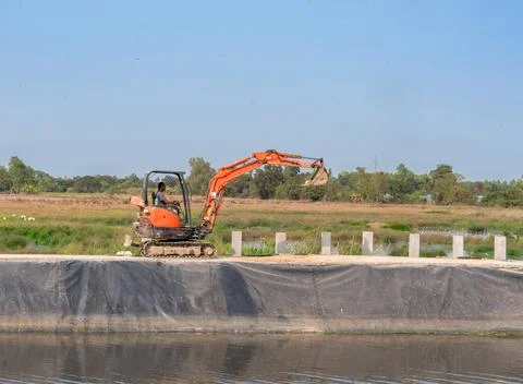 Small excavator working on pond edge for make fence. Stock Photos