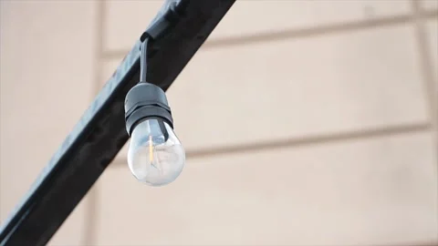 Small exterior outdoor string light bulb with black base hanging upside down Stock Footage 249754233
