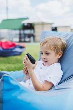 A small fair-haired boy of 5 years old sits in a chair on the street and lo.. Stock-Fotos