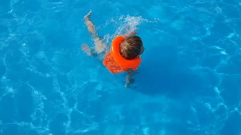 A small fair-haired boy swims in the pool of an aquapark in an inflatable Stock Footage 93775531