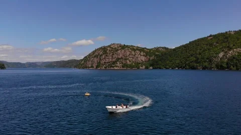 Small fast boat pulling a person on an inflatable ring in a fjord Stock Footage 334963132