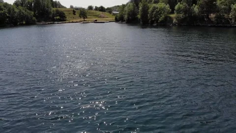 Small fast boat towing an inflatable ring with a person on it in a fjord Stock Footage 274708916