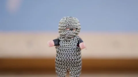 A small figure wearing a chain mail vest stands in front of a blue wall Stock Footage 298567825